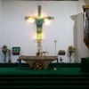 The sanctuary of Shrine of Mary, Queen of Peace, is primarily green in color; it has green carpet on the floor, the piano is covered in green, and the statue of Jesus on the crucifix at the center is a jade-colored stained glass with yellow lights at the back. The tabernacle is on the bottom-left of the crucifix (right if you are facing the congregation) and is covered with a jade-like slab. The walls are mostly dirty white marbles but look brown due to yellow lights. Also partly visible on the right (left if you are facing the congregation) are the organ with large silver pipes and a statue of Mary that looks like a smaller version of the one on top of the shrine.