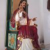 A statue of Jesus sitting on a green throne with goldtone decorations. Jesus is wearing red and white. His Sacred Heart is visible on his chest on the white part of his clothing.