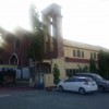 The external structure of Ina ng Laging Saklolo Parish as seen from an angle where the front and the right side is visible. The cross on top is not visible due to the glare produced by sun rays. While the front has a facade of maroon bricks, the side is mostly yellow. This shot was taken from the parking lot with the same elevation as the ground where the church stands.