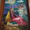 A portrait in Our Lady of the Annunciation Parish depicts Mary talking to Archangel Gabriel. Mary here is sitting wearing pink, yellow, and green. The dove-like Holy Spirit is also hovering above Mary.